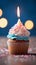 Birthday cupcake with burning candle, closeup, light background