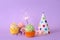 Birthday cupcakes with burning sparkler, party hat and gift box on violet background