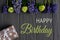 Birthday Greeting Card. Bright flowers and a box with a gift on a gray wooden background with the inscription. Ready-made greeting