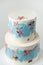 Birthday two tier cake with white chocolate frosting decorated with blue smears and multicolored pastel cream flowers on the white