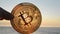 Bitcoin coin close up. Person holding Bitcoin coin on background sea shining sun
