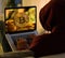 Bitcoin gold coin and anonymous hacker sittign with laptop.