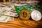 Bitcoins, circuit board and one hundred dollar bills on a wooden table