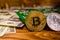 Bitcoins, circuit board and one hundred dollar bills on a wooden table