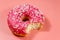 Bitten tasty pink donut on pink background
