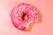 Bitten tasty pink donut on pink background. Top view