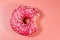 Bitten tasty pink donut on pink background. Top view
