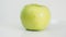 Bitten yellow green apple on white plate rotates