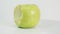 Bitten yellow green apple on white plate rotates