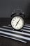 Black alarm clock on a black and white striped napkin showing 7 o`clock on a bedside table