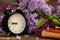 Black alarm clock, an old book and lilac flowers