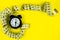 A black alarm clock stands on a bright yellow background surrounded by a measuring tape