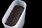 Black allspice in a plastic storage container on a black background, isolate.