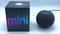 A black Apple Homepod Mini smart speaker with Siri being active next to its packaging on a bright background.
