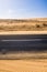 Black asphalt road with sand dunes and desert on left and right and blue sky in background  - travel concept in arid desertic