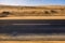 Black asphalt road with sand dunes and desert on left and right and blue sky in background  - travel concept in arid desertic