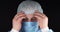 On a black background, the doctor pulls a surgical cap over his eyes from his head, expressing his fatigue. The surgeon