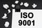 On a black background, there are crumpled pieces of paper and paper with the inscription -ISO 9001