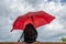 A black backpack protected by a red umbrella against a cloudy sky that threatens rain