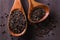 Black barley grains on wooden spoons over rustic wooden background