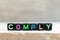 Black bead with letter in word comply on wood background