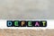 Black bead with letter in word defeat on wood background