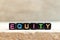 Black bead with letter in word equity on wood background