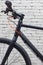 Black bicycle handlebar with speed switches, cables and brakes against a white brick wall.