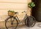 Black bicycle wicker basket with green composition on the trunk leaning against the beige wall