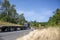 Black big rig classic style semi truck with empty flat bed semi trailer moving on the winding road with green trees on the side