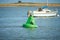 A black bird sitting on a water buoy. Green marker buoy floating in the sea. seagull, beacon. Sunny day summer.