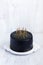 Black birthday cake with golden candles on white table