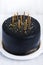 Black birthday cake with golden candles on white table