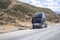 Black broken big rig semi truck tractor with open hood and with accident warning emergency signs standing on the road shoulder