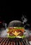 Black burger roasted on barbecue grill with flaming fire, sparks and smoke against black background. Beef cutlet, ham
