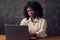 Black businesswoman with curly hair types on laptop lazily