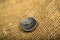 A black button sewn to a piece of burlap. Close up