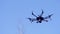 Black camera drone in flight with visible propelers movement and flashing light on blue sky background. Clip. Small