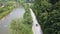 The black car is driving on good flat road near the river and thick green trees