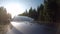 Black car driving on the highway with a snowy area and trees on both sides on a sunny day