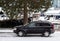 A black car parked outdoor on a street on a snowy winter day