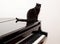 Black cat sitting on black piano with light background