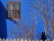 Black cat sitting in the sun on a picket fence in front of a blue wall with window