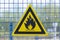 Black caution or warning fire triangle sign on yellow background or table on the painted fence grill