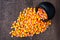 Black ceramic cauldron filled with holiday candy corn tipped over on a rustic wood background, spilling over onto the background