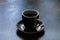 Black ceramic earthenware coffee cup on a saucer on a dark clean table