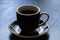 Black ceramic earthenware coffee cup on a saucer on a dark clean table