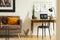 Black chair at desk with laptop and lamp next to couch in white workspace interior. Real photo