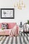 Black chair near pink couch in modern living room interior with poster and gold lamp. Real photo