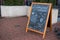 Black chalkboard in brown frame standing on paving slabs near by entrance of cafe with sentence